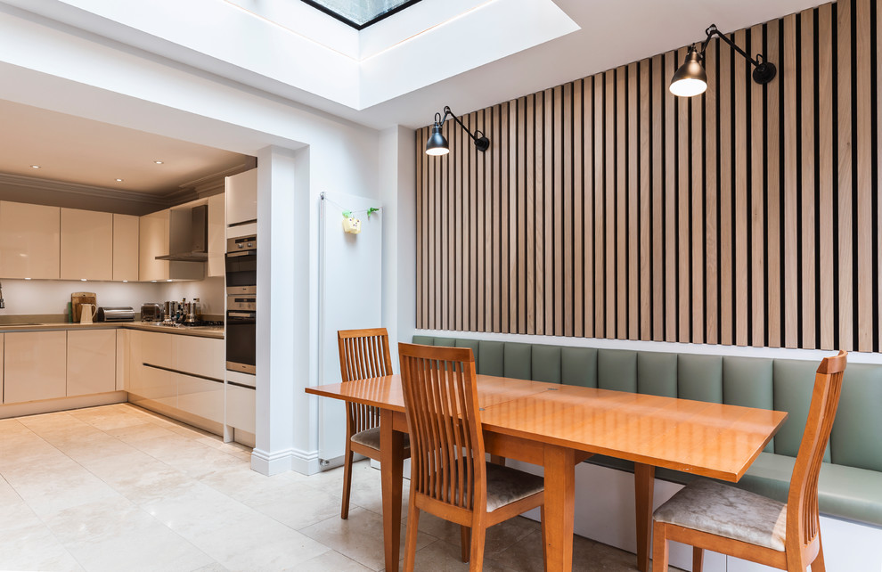 This is an example of a contemporary kitchen/dining room in London with white walls, no fireplace and beige floors.
