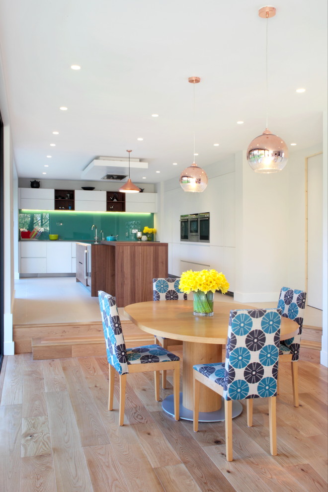 Cette photo montre une salle à manger ouverte sur la cuisine tendance avec un mur blanc et parquet clair.