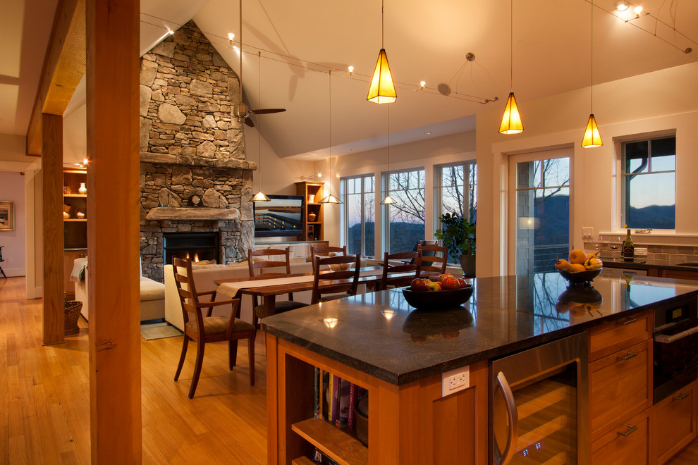 Exemple d'une grande salle à manger ouverte sur le salon craftsman avec un mur beige, un sol en bois brun, une cheminée standard et un manteau de cheminée en pierre.