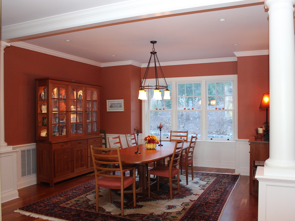 Cette image montre une grande salle à manger ouverte sur la cuisine traditionnelle avec un mur rouge et un sol en bois brun.