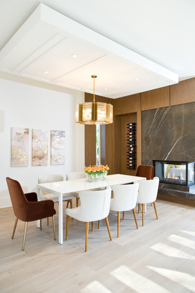 Design ideas for a medium sized contemporary open plan dining room in Vancouver with white walls, light hardwood flooring, a two-sided fireplace, a stone fireplace surround and brown floors.
