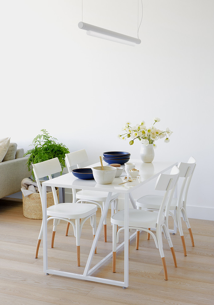 Bild på en liten minimalistisk matplats med öppen planlösning, med vita väggar, ljust trägolv, en dubbelsidig öppen spis, en spiselkrans i sten och beiget golv