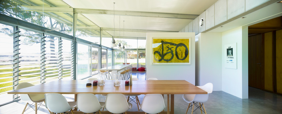 Aménagement d'une grande salle à manger ouverte sur la cuisine moderne avec un mur blanc et sol en béton ciré.
