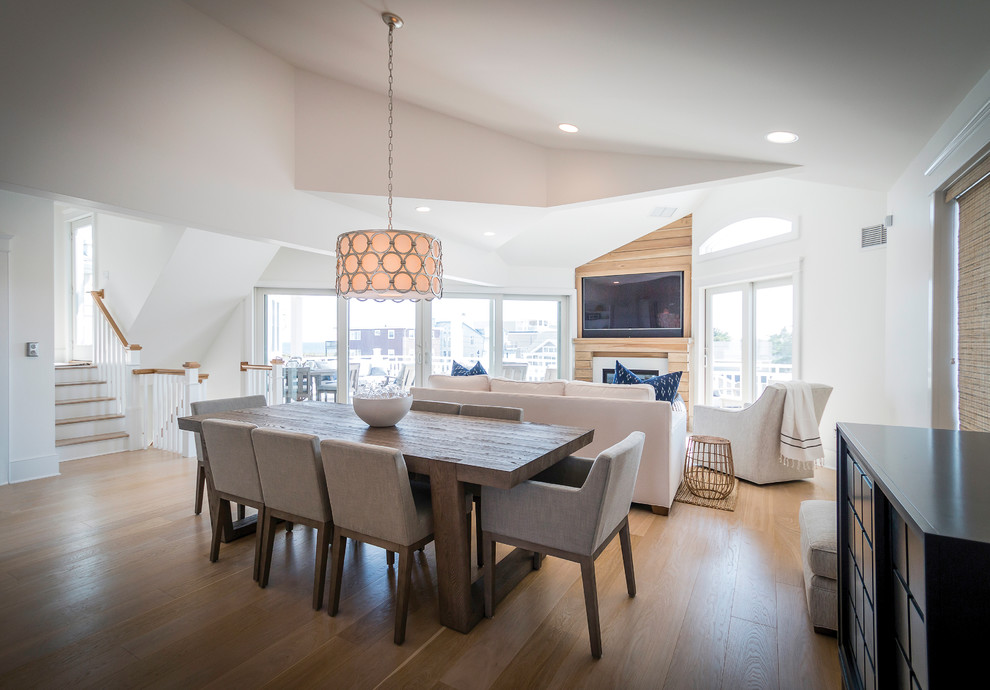 This is an example of an expansive coastal open plan dining room in New York with white walls and light hardwood flooring.