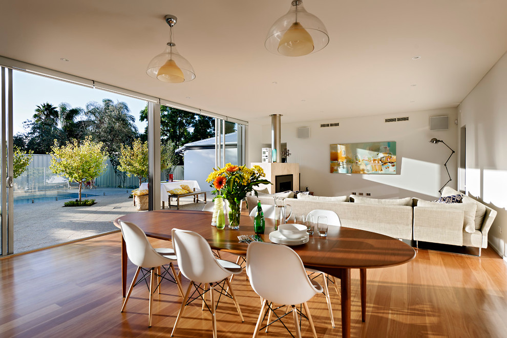Cette photo montre une salle à manger moderne avec un mur blanc, un sol en bois brun et éclairage.
