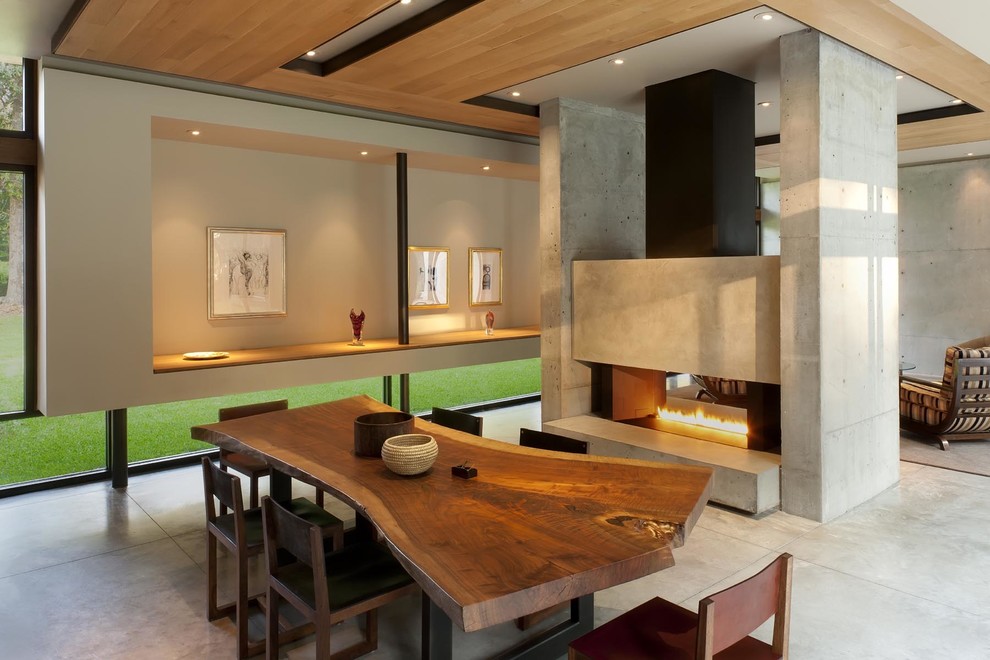 Ispirazione per una sala da pranzo aperta verso il soggiorno contemporanea con pareti beige, pavimento in cemento, camino bifacciale e cornice del camino in cemento