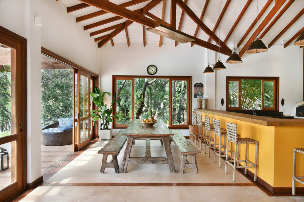 Immagine di una sala da pranzo aperta verso il soggiorno tropicale con pareti bianche, pavimento beige, travi a vista, soffitto in perlinato e soffitto a volta