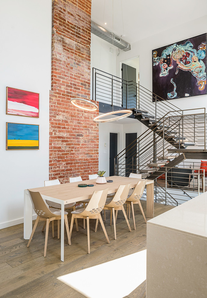 Idées déco pour une salle à manger ouverte sur la cuisine contemporaine de taille moyenne avec un mur blanc, un sol en bois brun, une cheminée standard, un manteau de cheminée en brique et un sol beige.