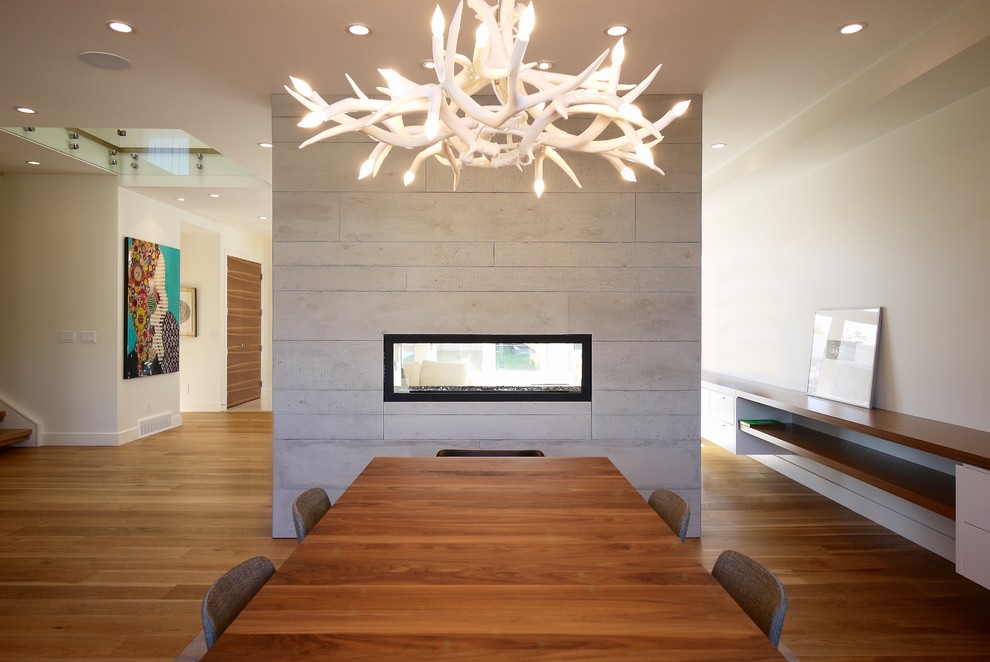 Imagen de comedor de cocina moderno de tamaño medio con paredes blancas, suelo de madera en tonos medios, chimenea de doble cara y marco de chimenea de hormigón
