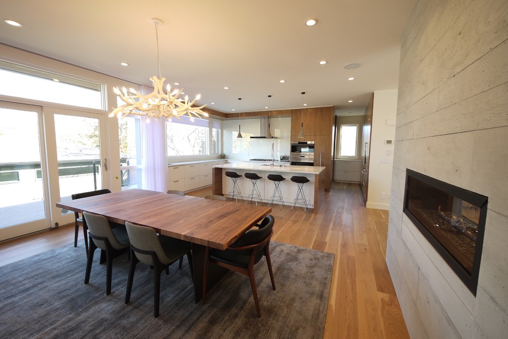 Idées déco pour une salle à manger ouverte sur la cuisine moderne de taille moyenne avec un mur blanc, un sol en bois brun, une cheminée double-face et un manteau de cheminée en béton.