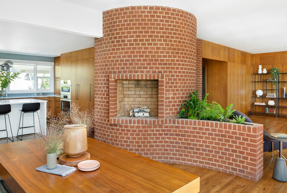 Réalisation d'une salle à manger ouverte sur la cuisine vintage avec un mur blanc, un sol en bois brun, un manteau de cheminée en brique et un sol marron.
