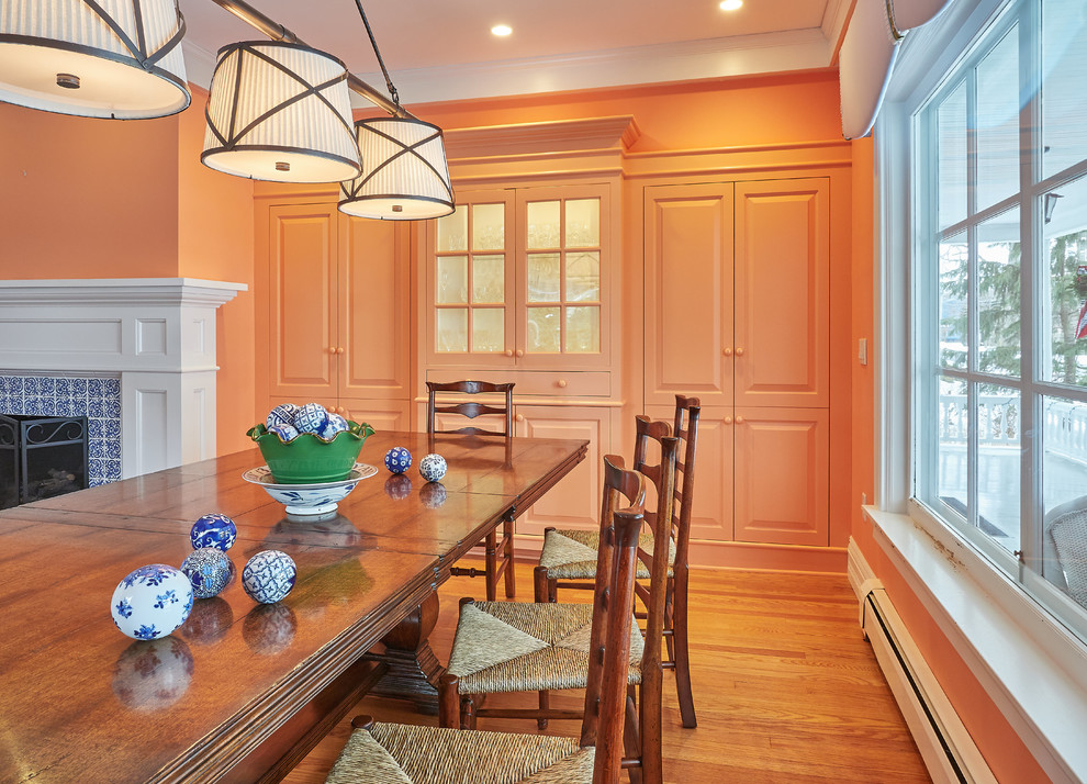 Réalisation d'une salle à manger ouverte sur le salon tradition de taille moyenne avec un mur orange, un sol en bois brun, une cheminée standard, un manteau de cheminée en carrelage et un sol marron.