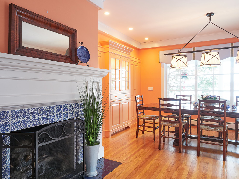Свежая идея для дизайна: гостиная-столовая среднего размера в стиле неоклассика (современная классика) с оранжевыми стенами, паркетным полом среднего тона, стандартным камином, фасадом камина из плитки и коричневым полом - отличное фото интерьера