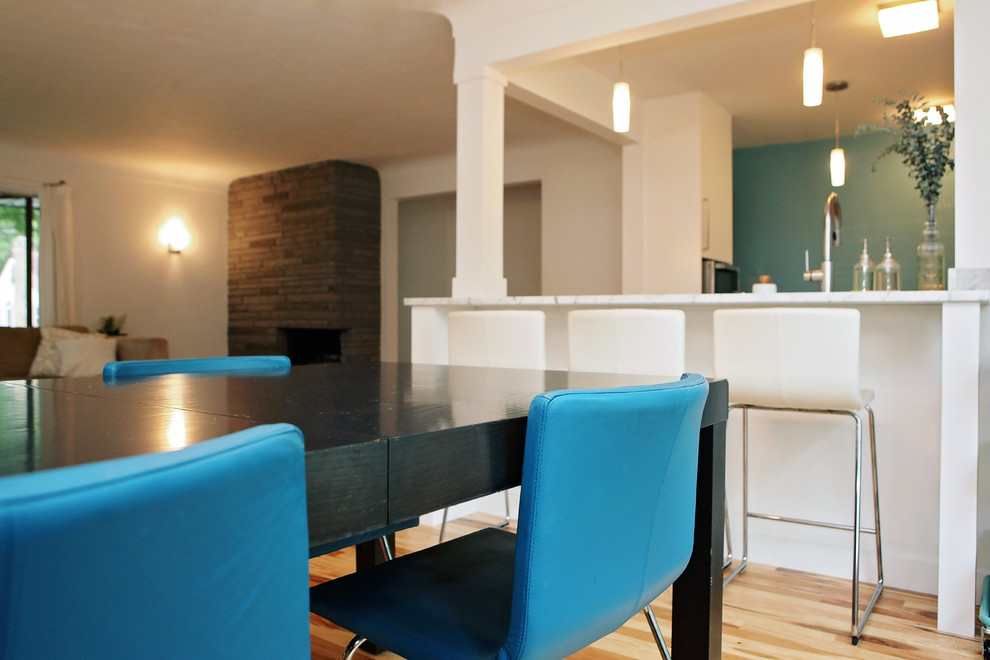 Aménagement d'une petite salle à manger ouverte sur le salon contemporaine avec un mur blanc, un sol en bois brun, une cheminée standard et un manteau de cheminée en pierre.
