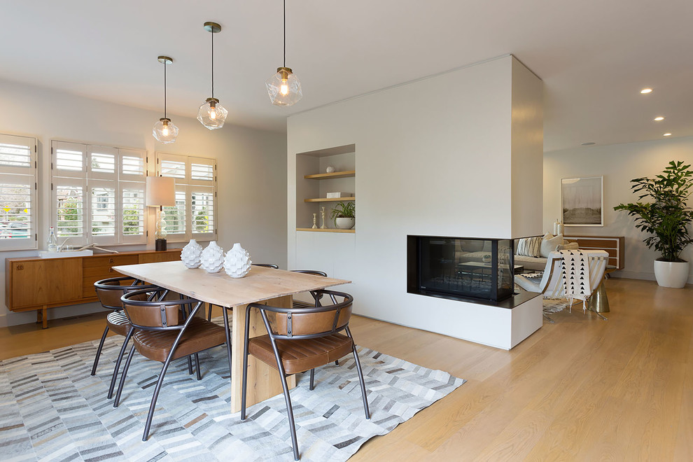 This is an example of a large midcentury open plan dining room in San Francisco with grey walls, light hardwood flooring, a two-sided fireplace and feature lighting.