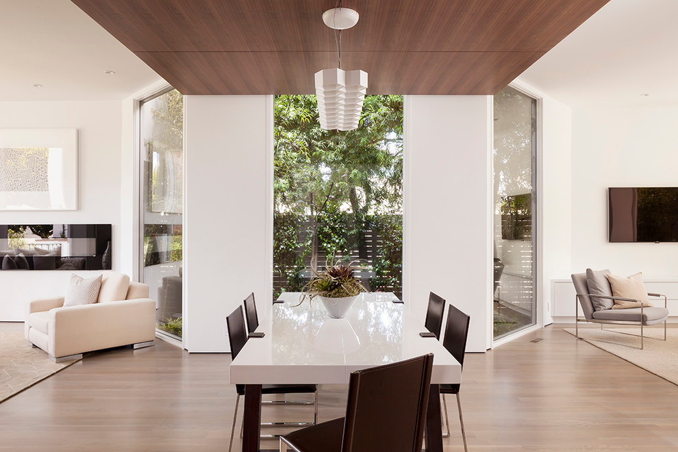 Réalisation d'une salle à manger ouverte sur le salon design avec un mur blanc et parquet clair.