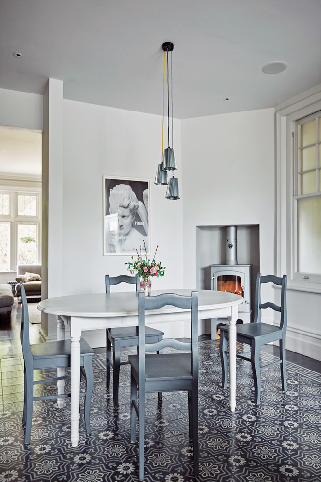 Example of a transitional dining room design in London with white walls and a wood stove