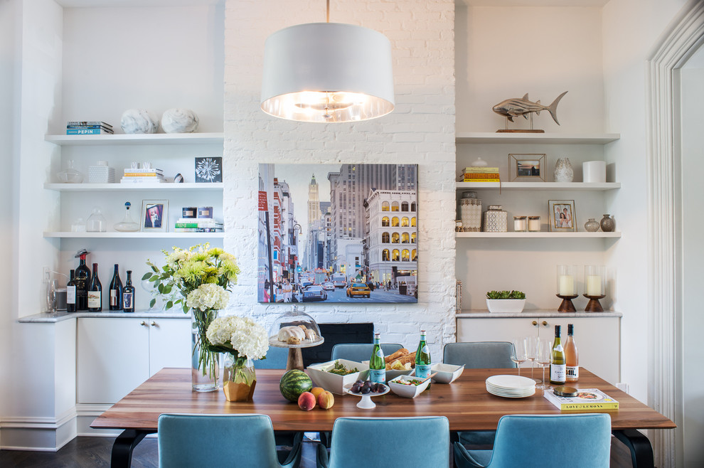 Idée de décoration pour une salle à manger ouverte sur la cuisine design de taille moyenne avec un mur blanc, parquet foncé, une cheminée standard, un manteau de cheminée en brique et un sol noir.