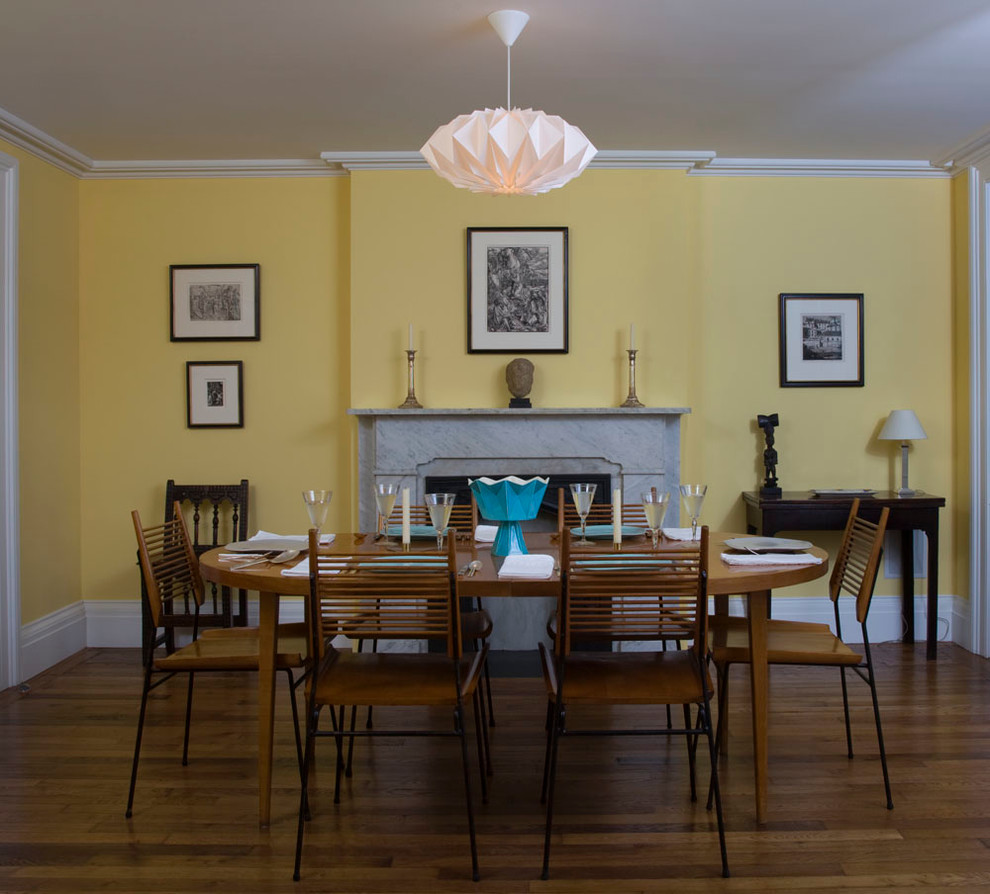 Immagine di una sala da pranzo classica chiusa e di medie dimensioni con pareti gialle, pavimento in legno massello medio, camino classico e cornice del camino in pietra