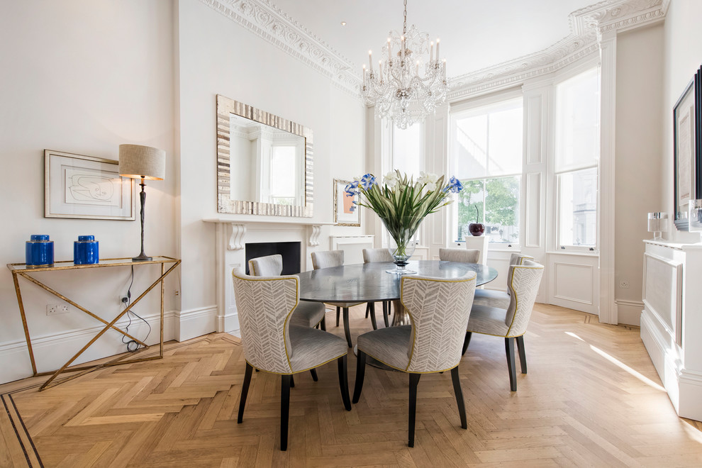 Classic dining room in London with white walls, light hardwood flooring, a standard fireplace and feature lighting.