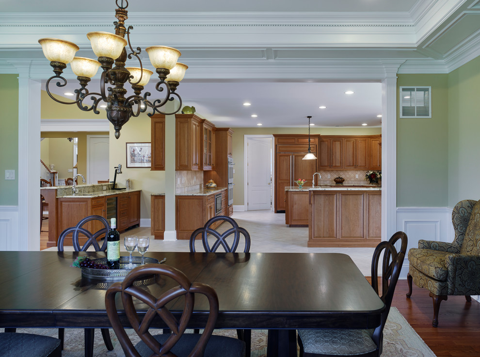 Foto di una grande sala da pranzo aperta verso la cucina classica con pareti verdi, pavimento in legno massello medio, camino classico e cornice del camino in pietra