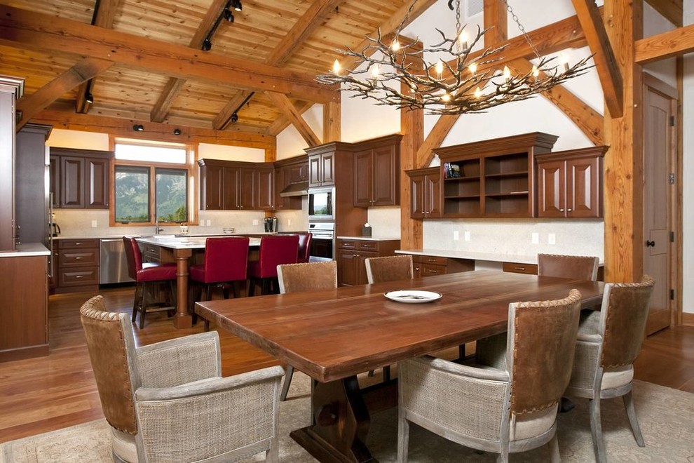Cette photo montre une grande salle à manger montagne avec un mur blanc, un sol en bois brun, une cheminée standard, un manteau de cheminée en pierre et un sol marron.