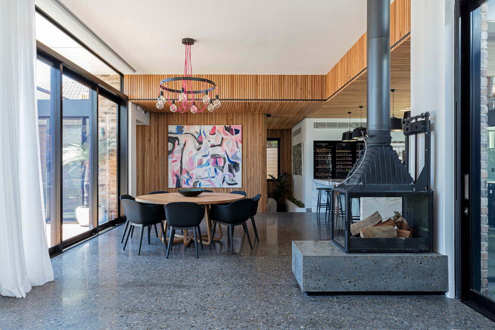 Idée de décoration pour une salle à manger design avec sol en béton ciré, un mur blanc, un poêle à bois et un manteau de cheminée en métal.