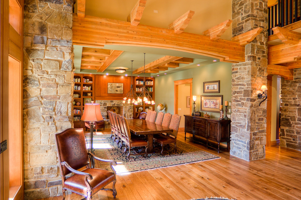 Cette image montre une grande salle à manger ouverte sur le salon chalet avec un mur vert, un sol en bois brun, une cheminée standard et un manteau de cheminée en pierre.