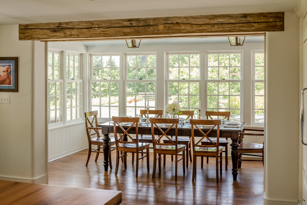 Cette image montre une salle à manger ouverte sur la cuisine rustique avec un mur blanc et un sol en bois brun.
