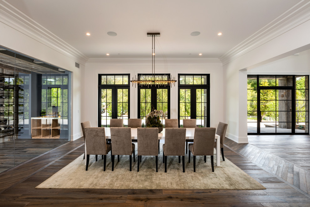 Cette photo montre une grande salle à manger ouverte sur le salon chic avec un mur blanc et un sol en bois brun.