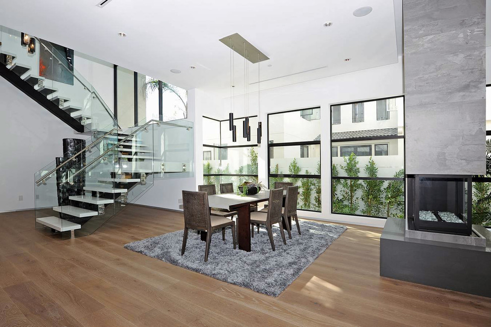 Cette photo montre une grande salle à manger ouverte sur le salon moderne avec un mur blanc, un sol en bois brun et une cheminée d'angle.
