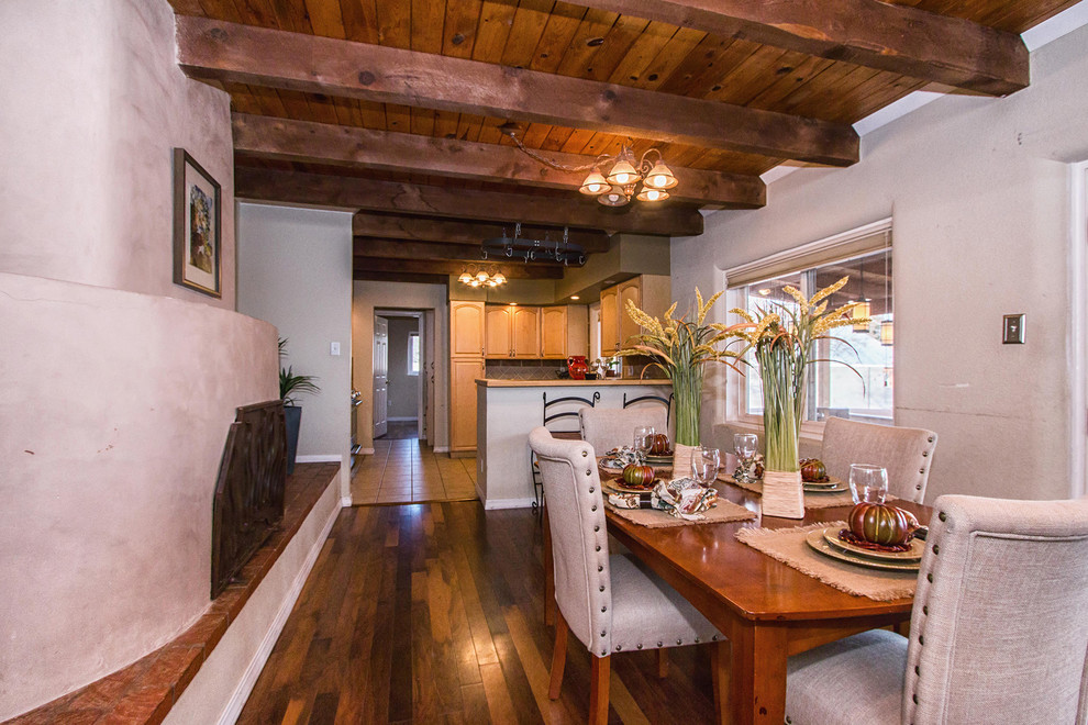 Cette image montre une grande salle à manger ouverte sur la cuisine sud-ouest américain avec un mur blanc, un sol en bois brun, une cheminée standard et un manteau de cheminée en brique.