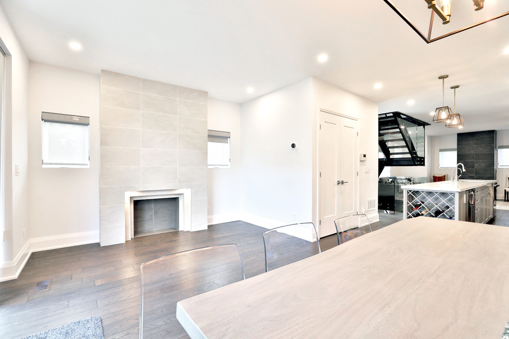 Cette photo montre une salle à manger ouverte sur la cuisine moderne de taille moyenne avec un mur blanc, parquet foncé, une cheminée standard et un manteau de cheminée en carrelage.