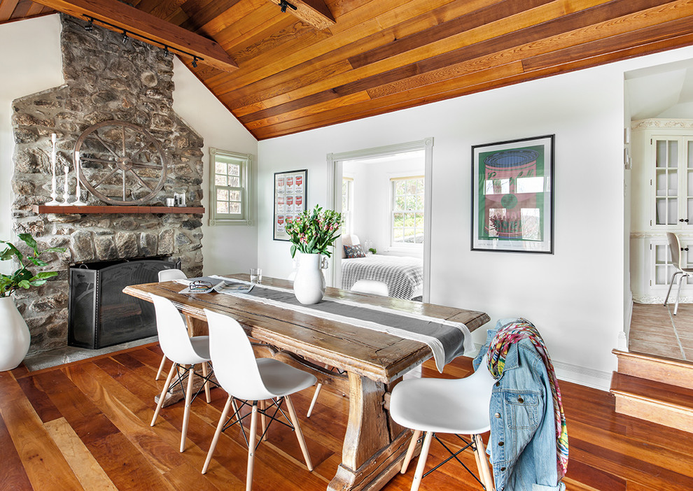 Cette photo montre une salle à manger ouverte sur la cuisine tendance de taille moyenne avec un mur blanc, un sol en bois brun, une cheminée standard et un manteau de cheminée en pierre.