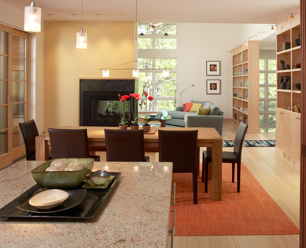 This is an example of a medium sized contemporary kitchen/dining room in Boston with yellow walls, light hardwood flooring, a two-sided fireplace, a tiled fireplace surround and beige floors.