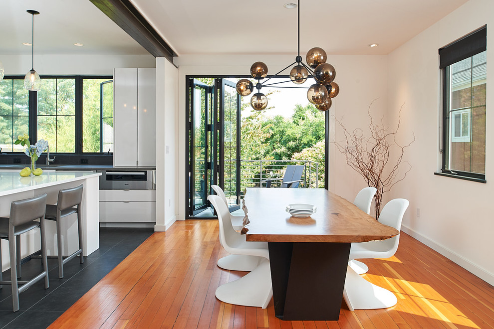 Cette photo montre une salle à manger ouverte sur la cuisine tendance avec un mur blanc, un sol en bois brun et un sol marron.