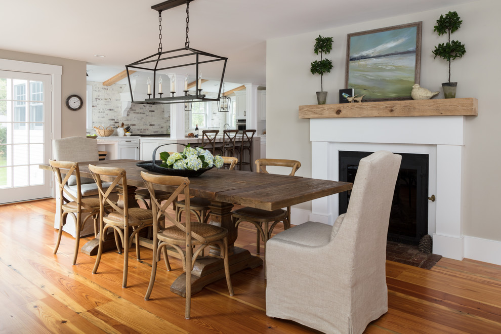 Cette photo montre une salle à manger ouverte sur la cuisine nature de taille moyenne avec un mur beige, un sol en bois brun, une cheminée standard, un manteau de cheminée en plâtre et un sol marron.