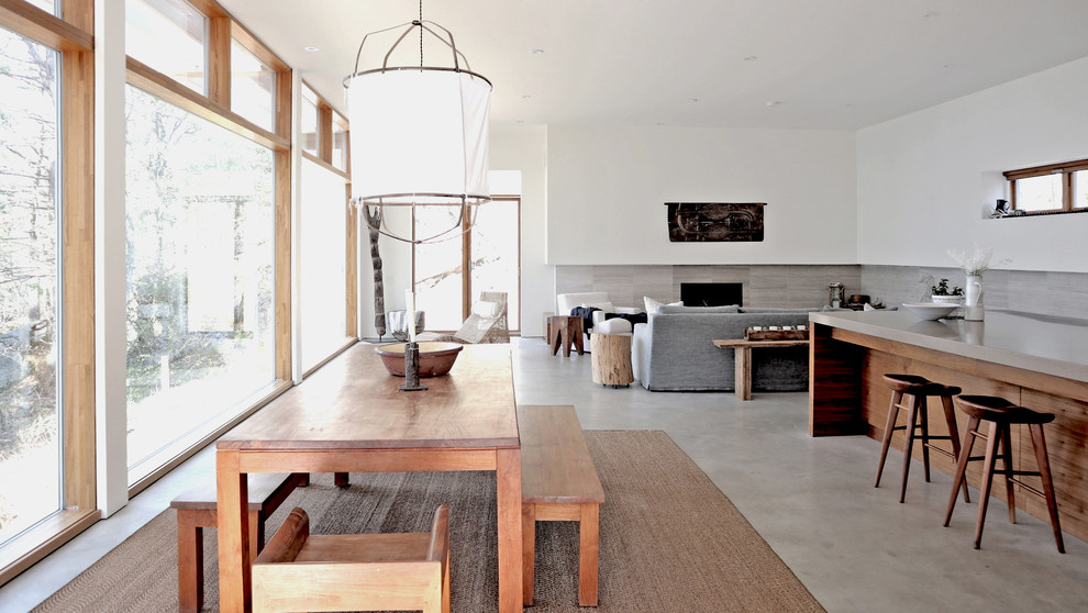 Стильный дизайн: огромная гостиная-столовая в современном стиле с белыми стенами, бетонным полом, стандартным камином, фасадом камина из плитки и серым полом - последний тренд