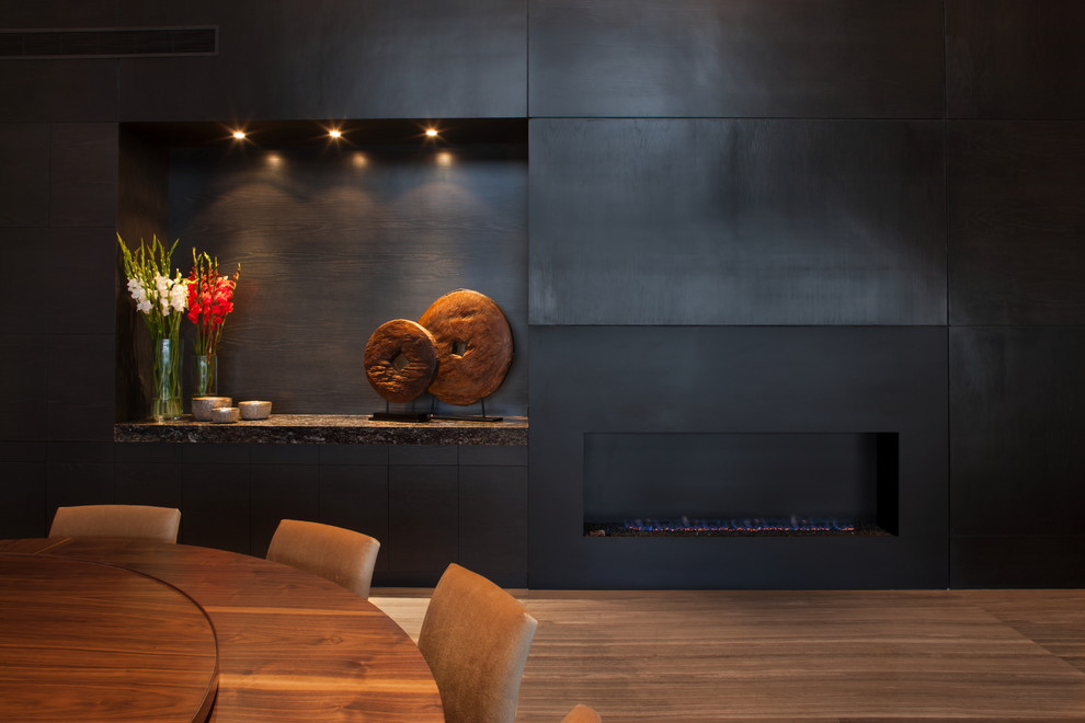 Idée de décoration pour une salle à manger design avec un mur noir, parquet foncé et une cheminée ribbon.