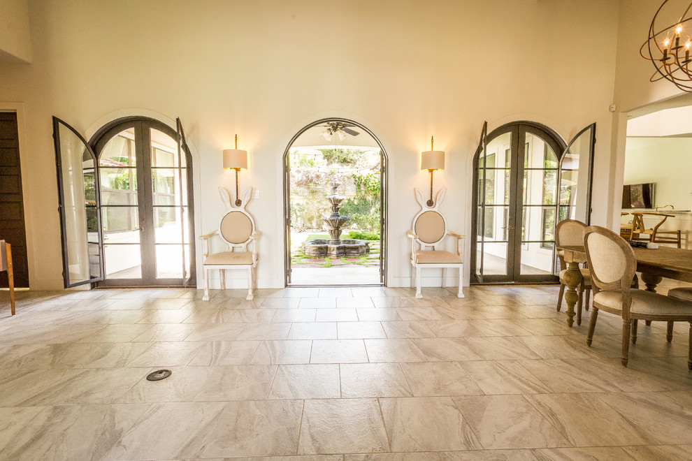 Esempio di una grande sala da pranzo mediterranea con pareti bianche, pavimento in gres porcellanato, camino bifacciale, cornice del camino in pietra e pavimento grigio