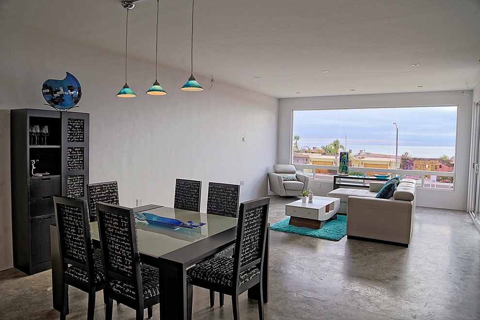 Cette image montre une salle à manger ouverte sur le salon design avec un mur gris, sol en béton ciré, une cheminée double-face et un manteau de cheminée en béton.