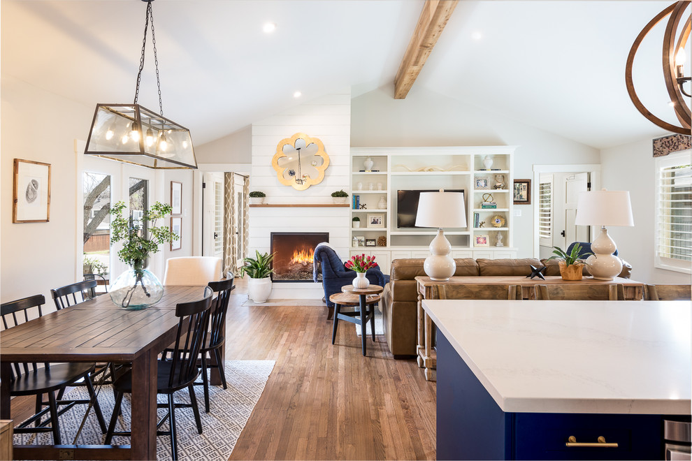 Cette photo montre une salle à manger ouverte sur le salon tendance de taille moyenne avec une cheminée standard, un sol marron, un mur beige, parquet foncé et un manteau de cheminée en bois.