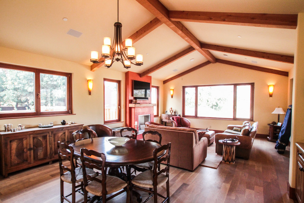 Cette photo montre une salle à manger ouverte sur le salon méditerranéenne de taille moyenne avec un mur beige, un sol en bois brun, une cheminée standard, un manteau de cheminée en plâtre et un sol marron.