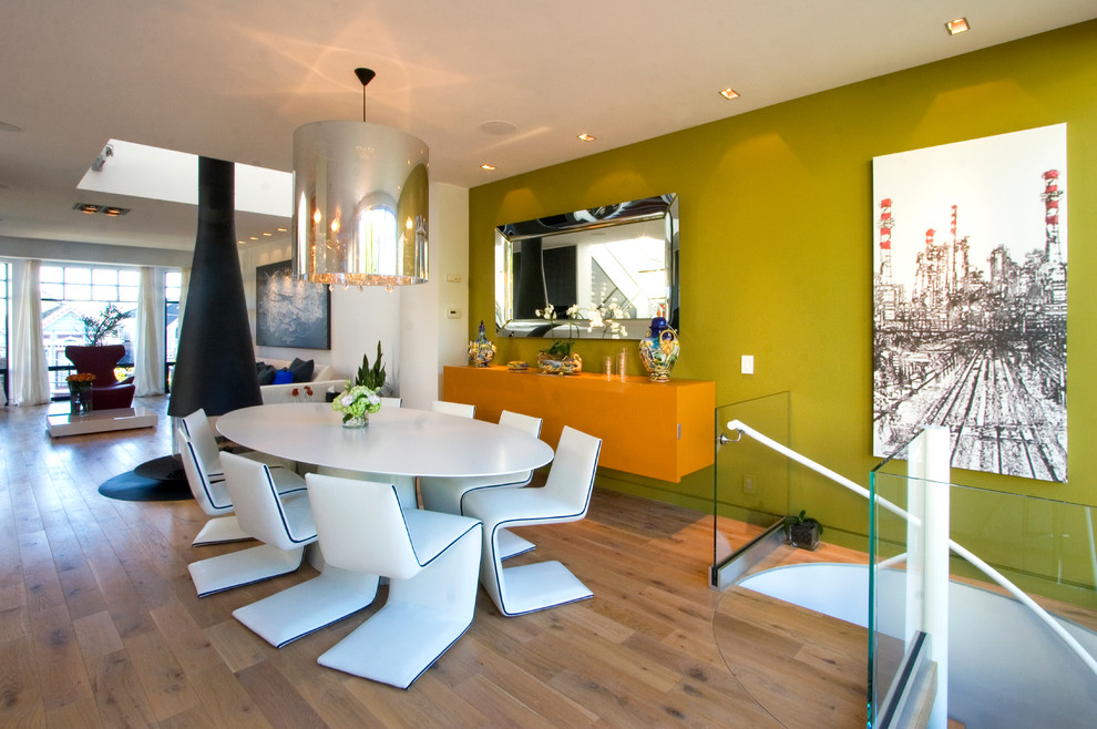 Cette photo montre une salle à manger ouverte sur le salon tendance de taille moyenne avec un mur vert, un sol en bois brun, un manteau de cheminée en métal et cheminée suspendue.