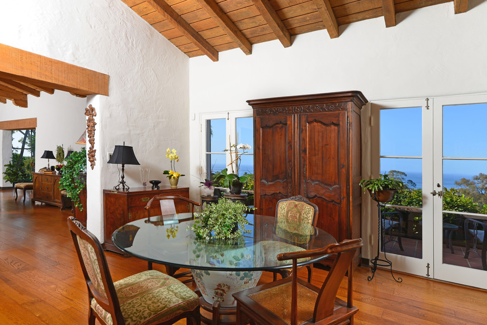 Aménagement d'une salle à manger méditerranéenne avec un mur blanc et un sol en bois brun.