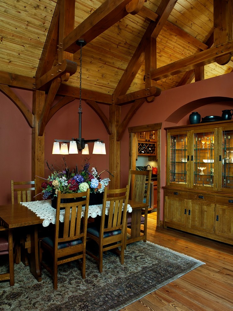 Cette photo montre une grande salle à manger montagne avec parquet clair, une cheminée double-face, un manteau de cheminée en pierre et un mur rouge.
