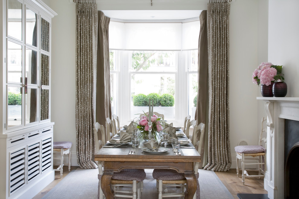 Immagine di una sala da pranzo tradizionale con pareti bianche, parquet chiaro e camino classico