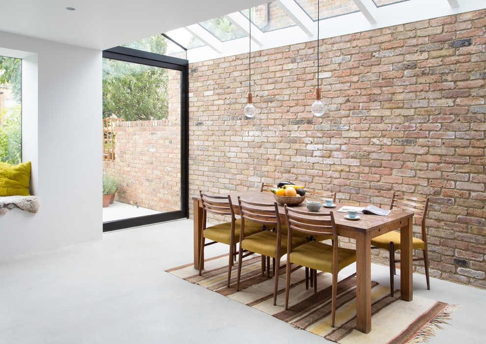 Immagine di una sala da pranzo aperta verso la cucina scandinava di medie dimensioni con pareti marroni, pavimento in cemento, pavimento grigio e pareti in mattoni