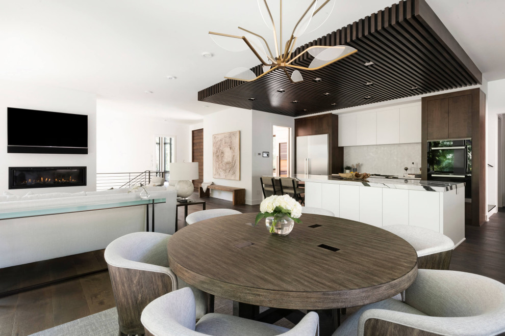 На фото: кухня-столовая в стиле модернизм с белыми стенами, темным паркетным полом, стандартным камином и фасадом камина из металла с