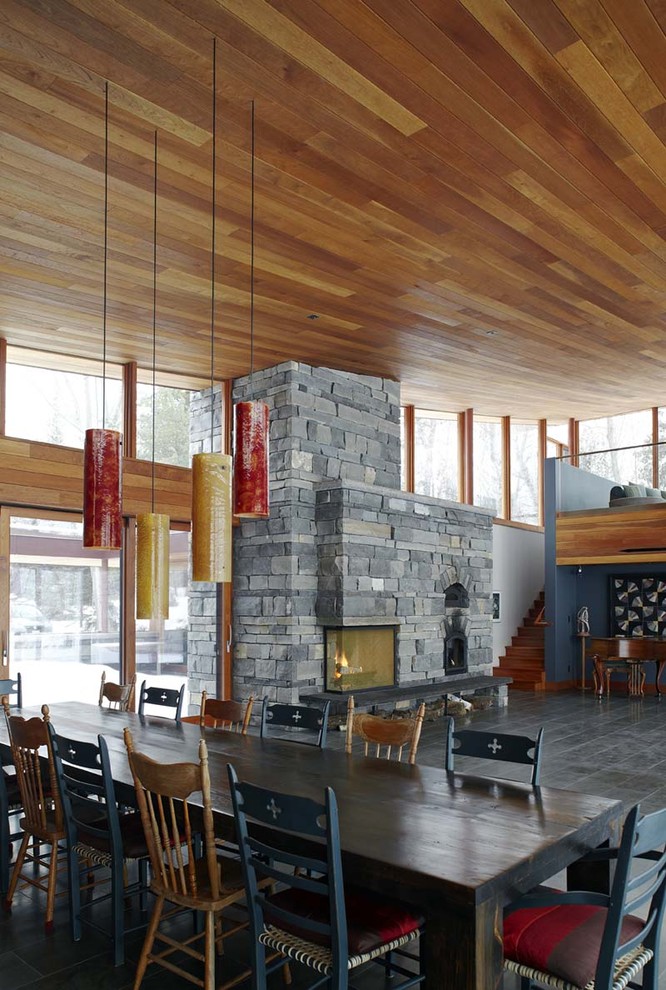 Cette photo montre une grande salle à manger ouverte sur le salon tendance avec un sol en ardoise, un manteau de cheminée en pierre et une cheminée standard.